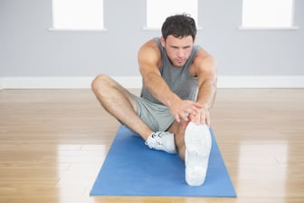 Attractive sporty man stretching his right leg in bright room