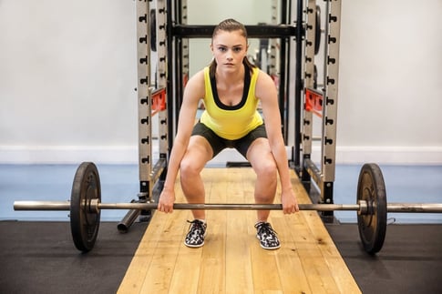 Concentrated woman about to lift a barbell and weights at the gym